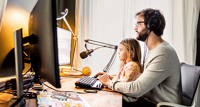 Man with headphones sitting at desk with little girl in his lap