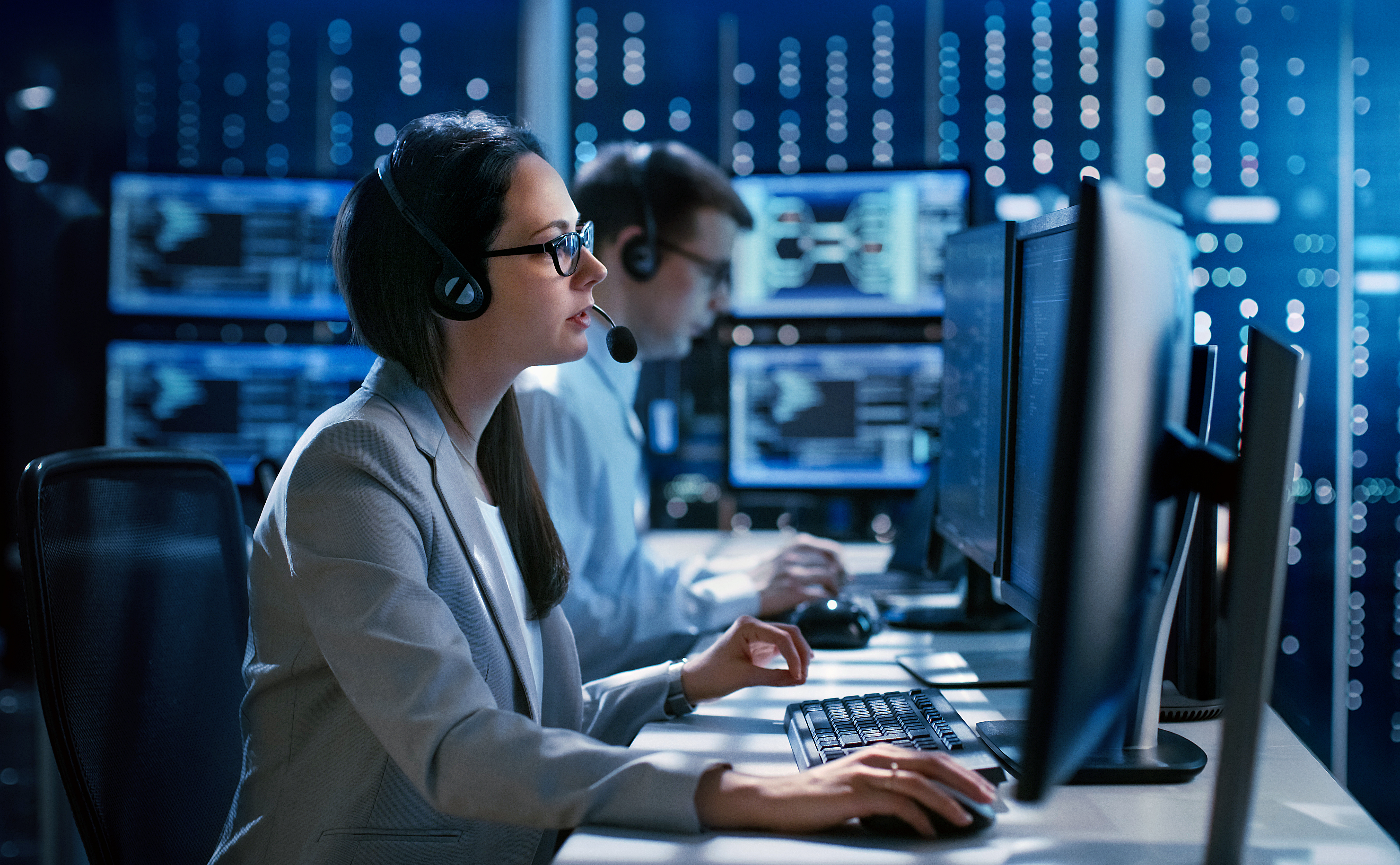 Two people wearing headsets on computers with blurred out background