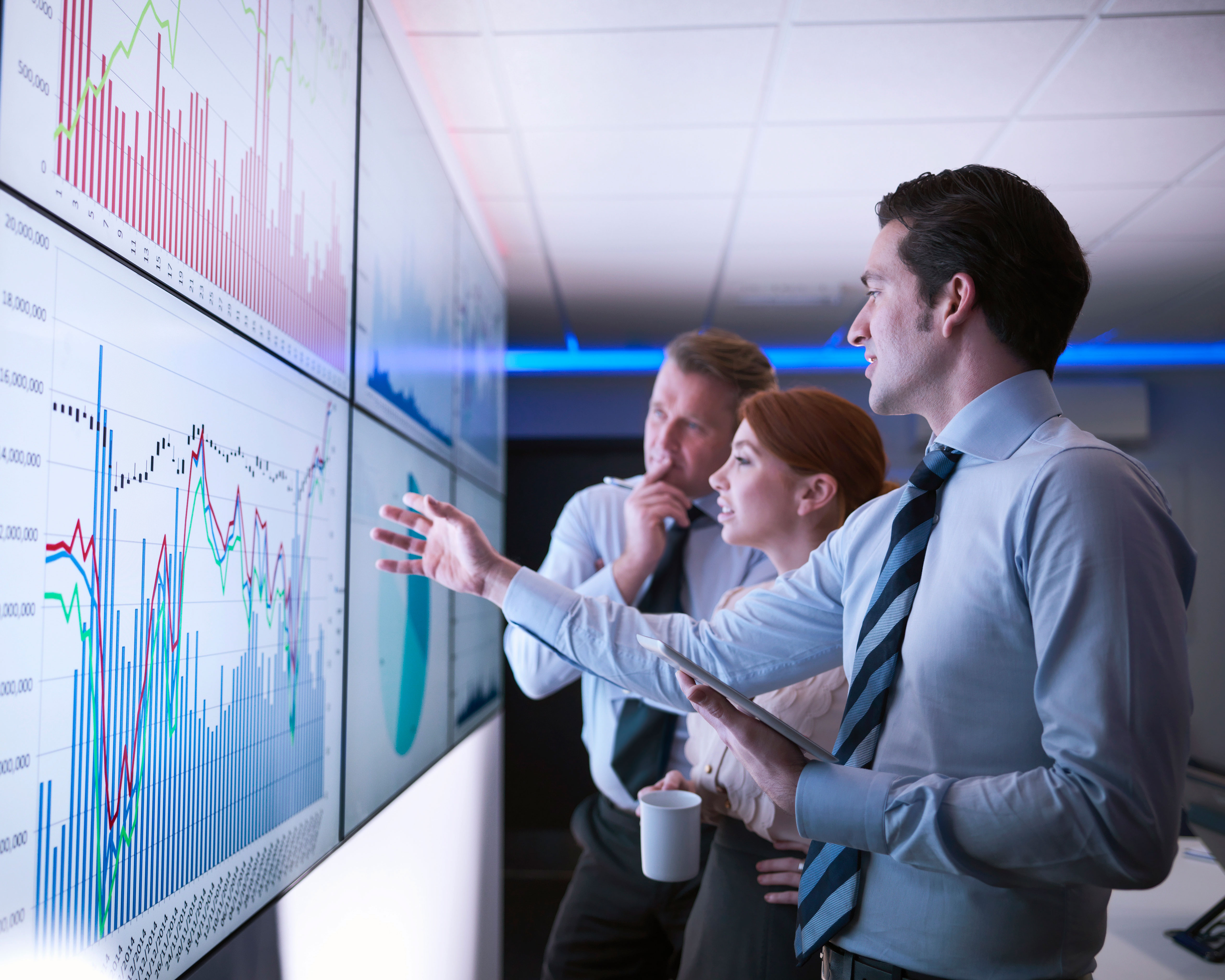 Three people working in front of big screen with data