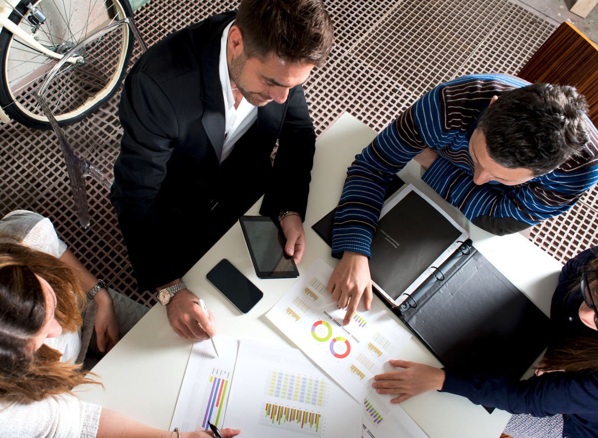 a group of colleagues sitting at a table looking over data sheets with graphs and charts 