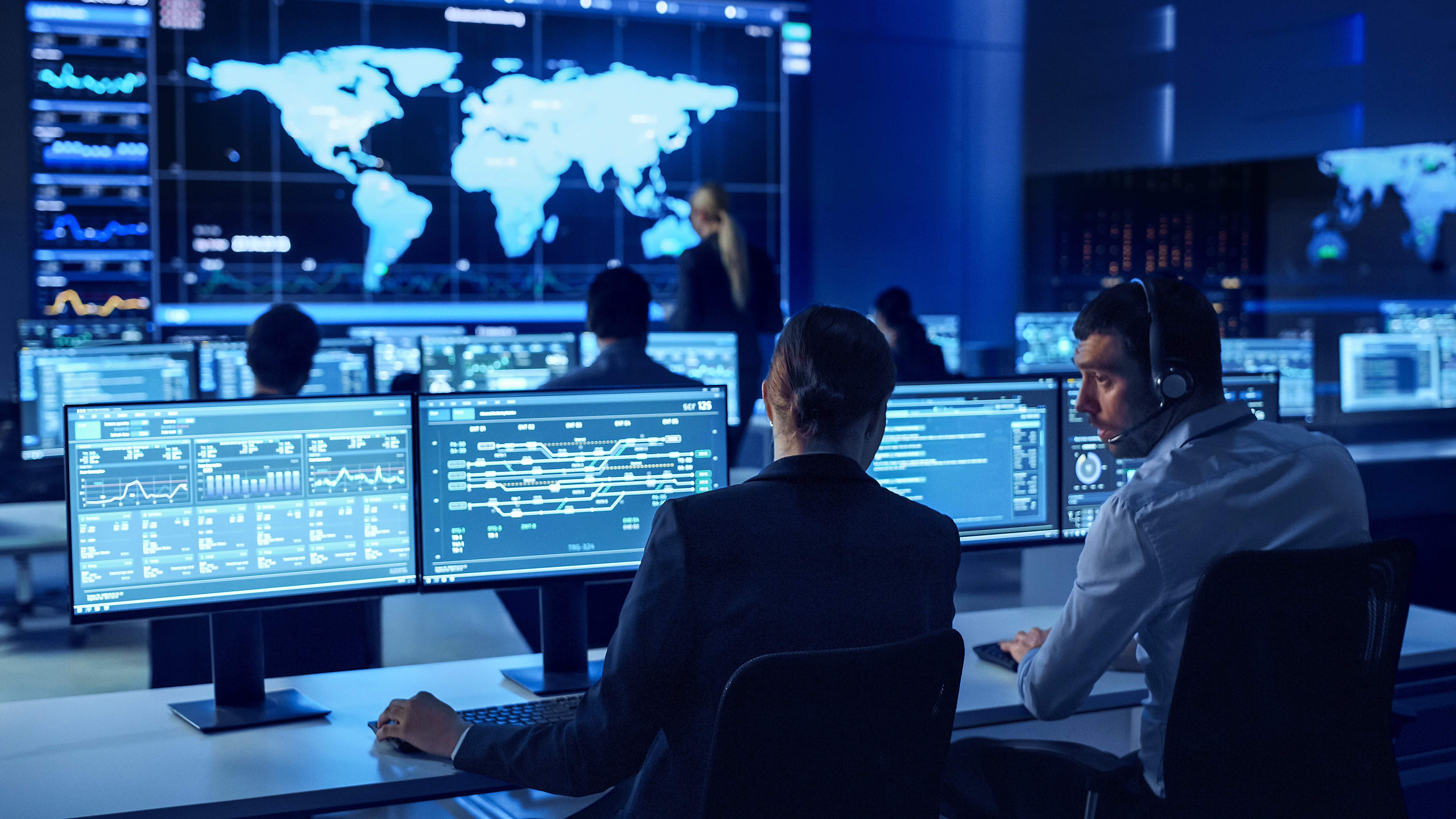 two people sitting next to each other in front of multiple computer monitors